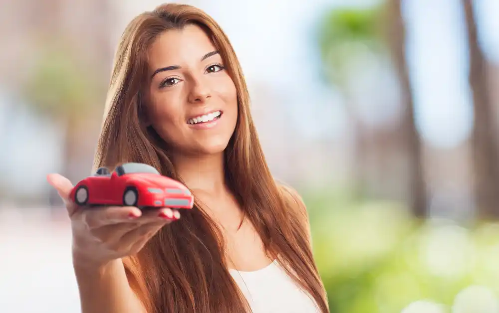 Mulher segurando uma miniatura de carro na mão ilustrando a dúvida se deve contratar uma proteção veicular ou seguro auto.