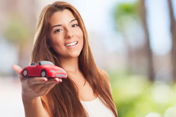 Mulher segurando uma miniatura de carro na mão ilustrando a dúvida se deve contratar uma proteção veicular ou seguro auto.