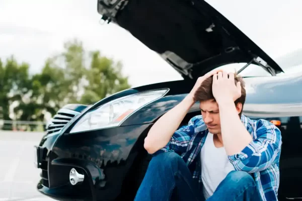 Um homem decepcionado por não ser aceito no seguro alto sentado no chão ao lado do carro.